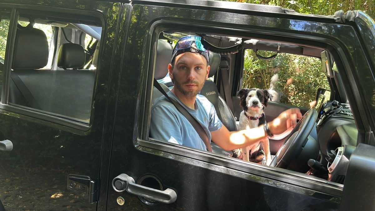 Allan Perrottet in the driver's seat of his black 2014 Jeep Wrangler Unlimited on a wooded trail, with his dog Zoé beside him